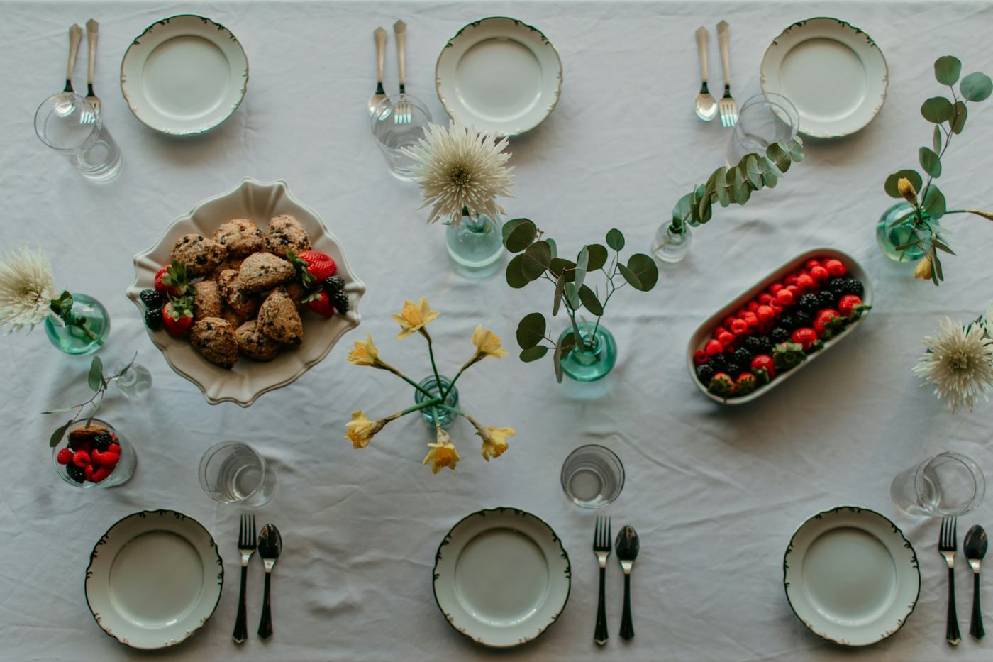 Mesa posta vista de cima com toalha branca, pratos, flores amarelas e travessas