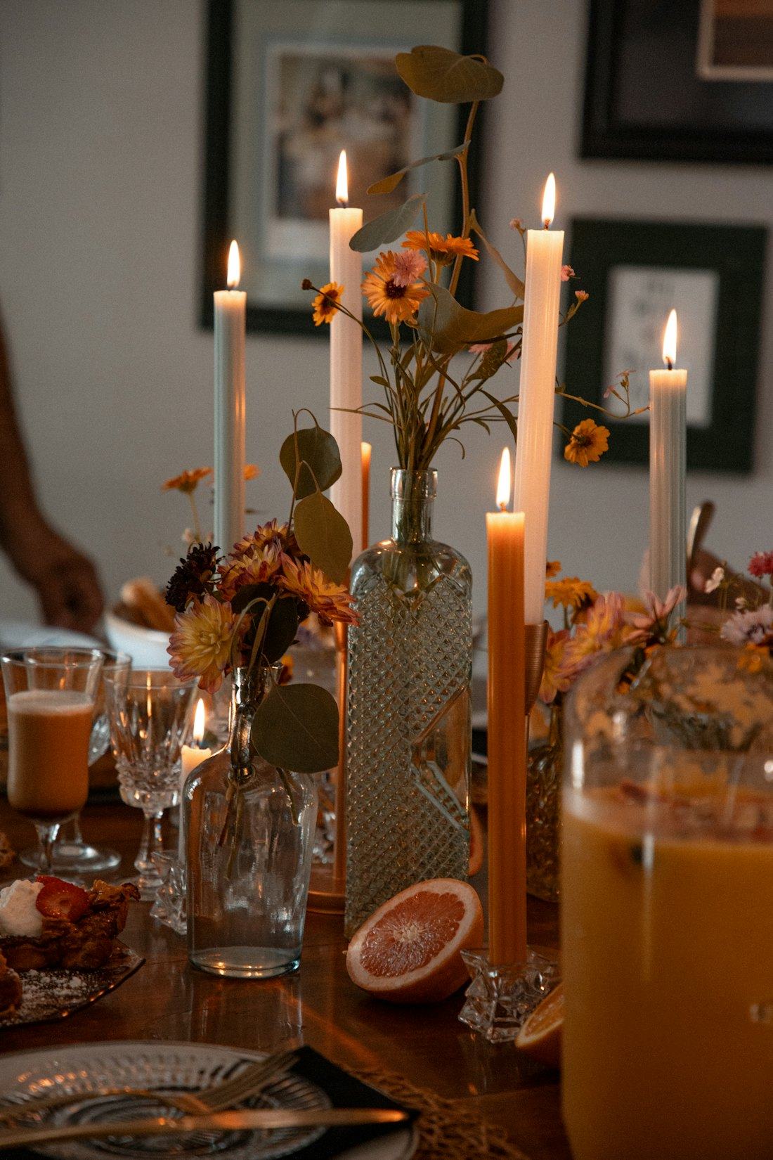 Mesa longa de jantar com velas acesas, flores secas e taças