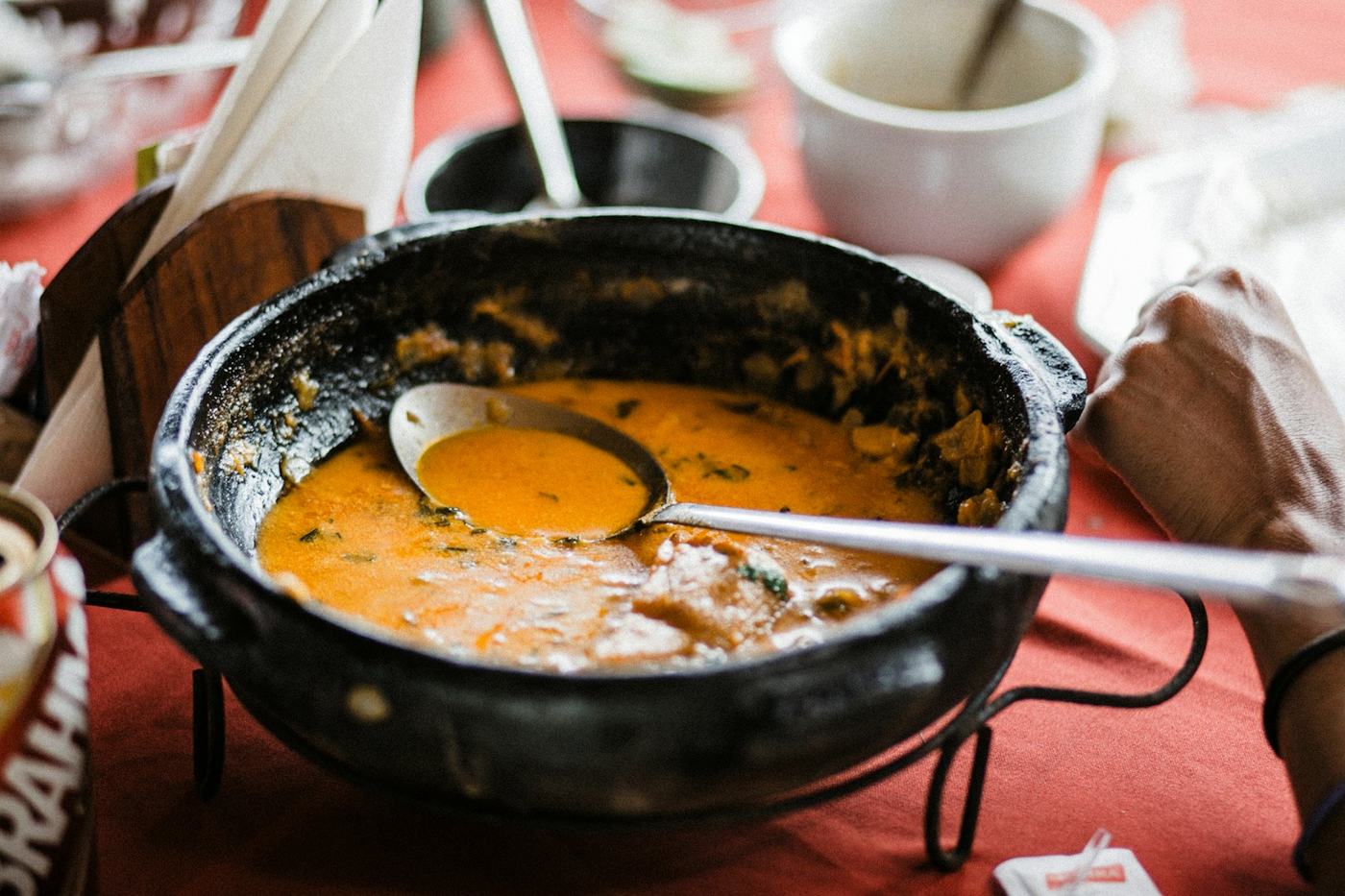 Panela de ferro com moqueca de caldo alaranjado e uma concha, sobre toalha vermelha